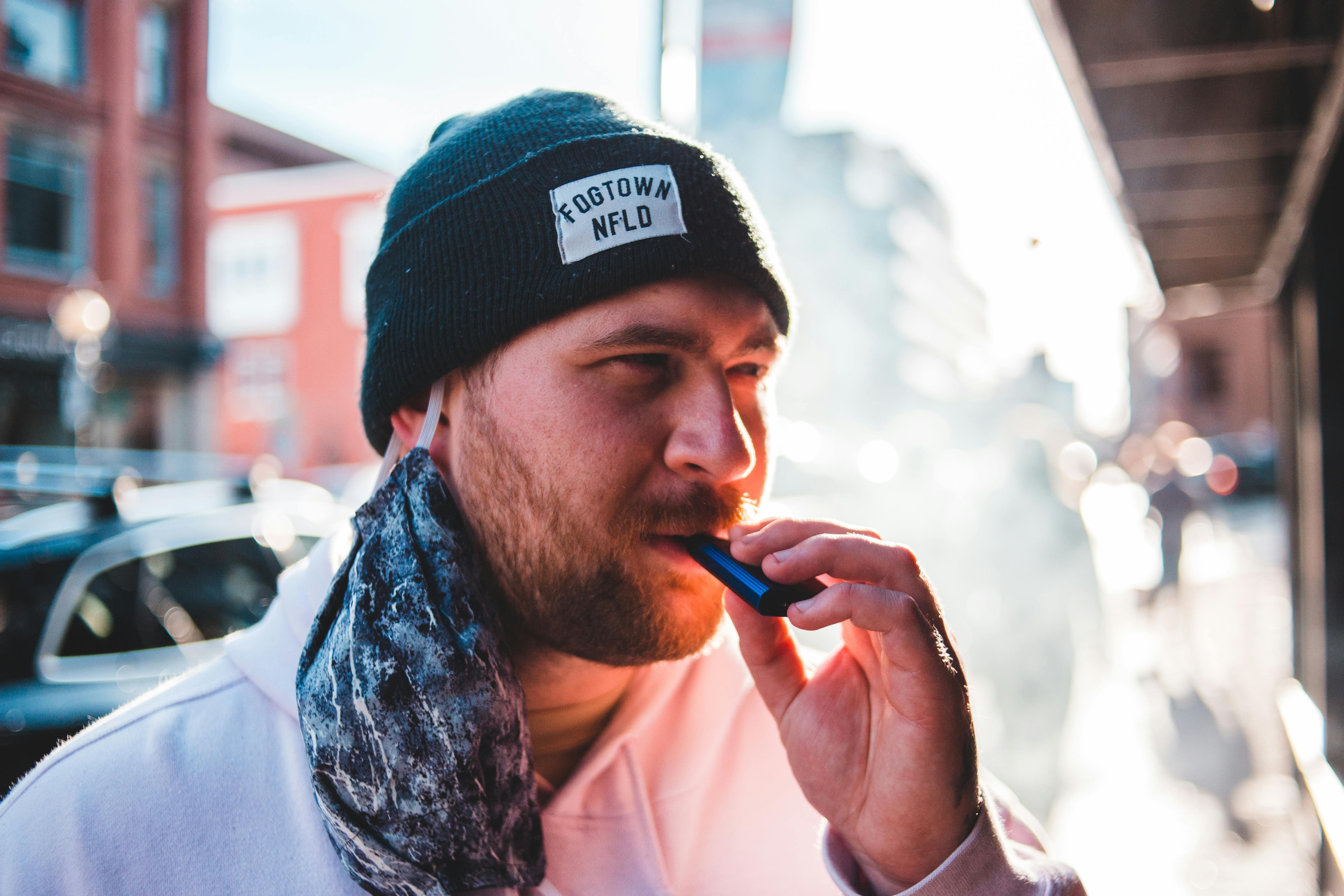 man in a beanie vaping from a device