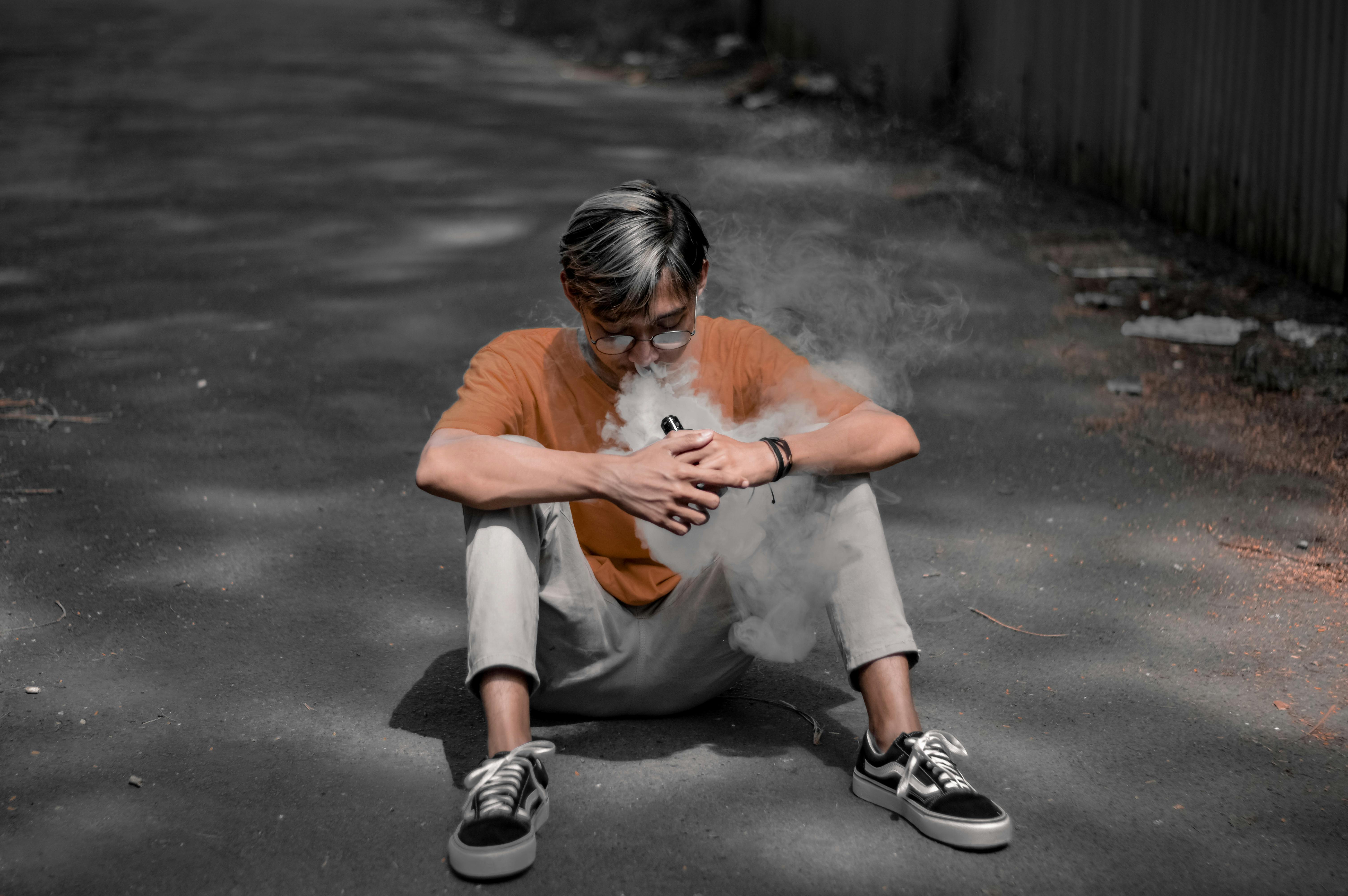 man sitting on a road and vaping
